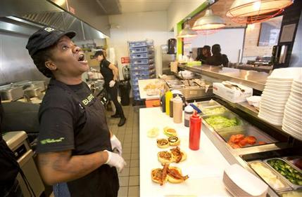 In this Tuesday, Jan. 27, 2015 photo, BurgerFi restaurant employee Nathali Dorvil calls out an order as Elia Carranza, rear, mans the grill at the Aventura, Fla., restaurant. The company plans to nearly double in size from their existing 65 restaurants this year. (AP Photo/Wilfredo Lee)