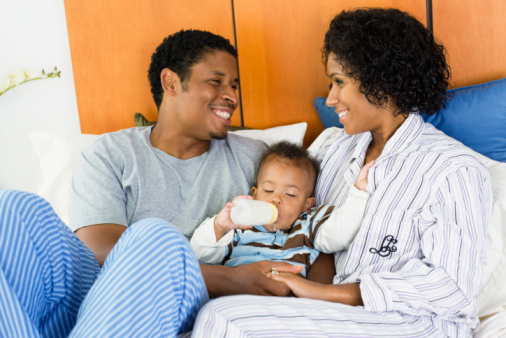 African parents feeding child bottle in bed
