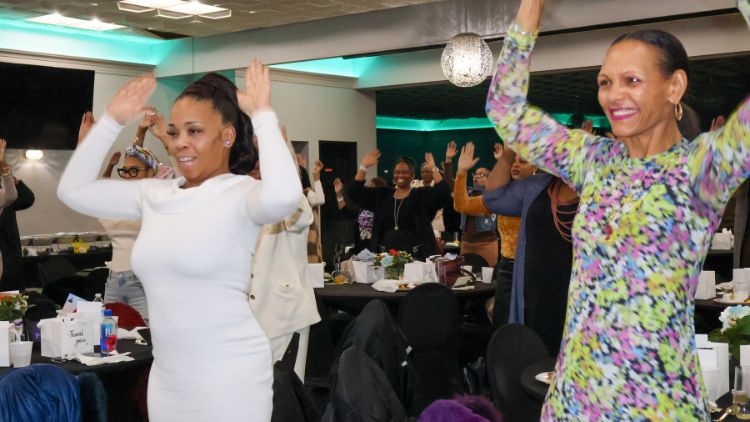 ModeratorHFCC founderchair Tanya Bennett and the room of attendees standing up to exercise (Photo Provided).