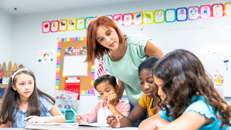 A young female teacher monitors students working on a writing lesson.