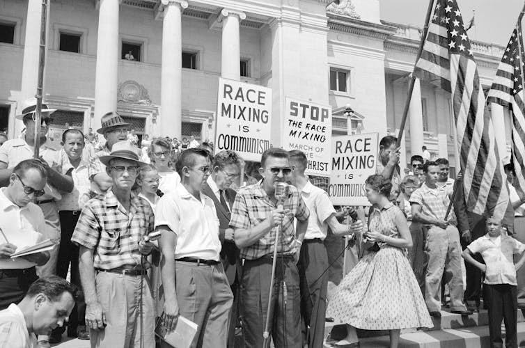 Crowd at Arkansas State Capitol protesting integration, with signs reading 'Race mixing is Communism' and 'Stop the race mixing.'
